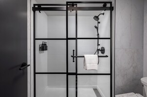 Un baño moderno con ducha acristalada, azulejos blancos y estructura de metal negro.