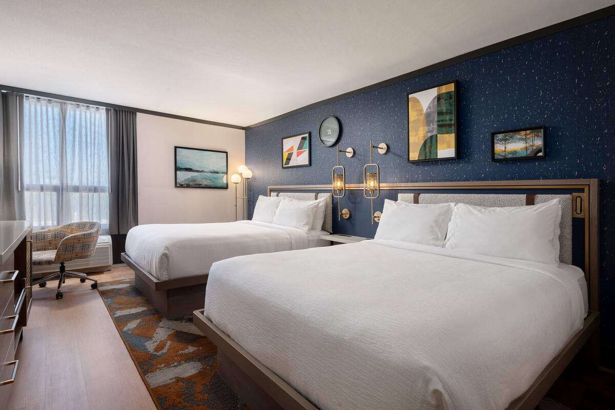 Ein Hotelzimmer mit zwei Betten, einem Schreibtisch, einem Sessel und Bildern an den Wänden.