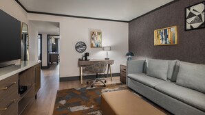 Un salon moderne avec un canapé gris, un bureau avec une chaise, un téléviseur et des œuvres d’art accrochées aux murs.