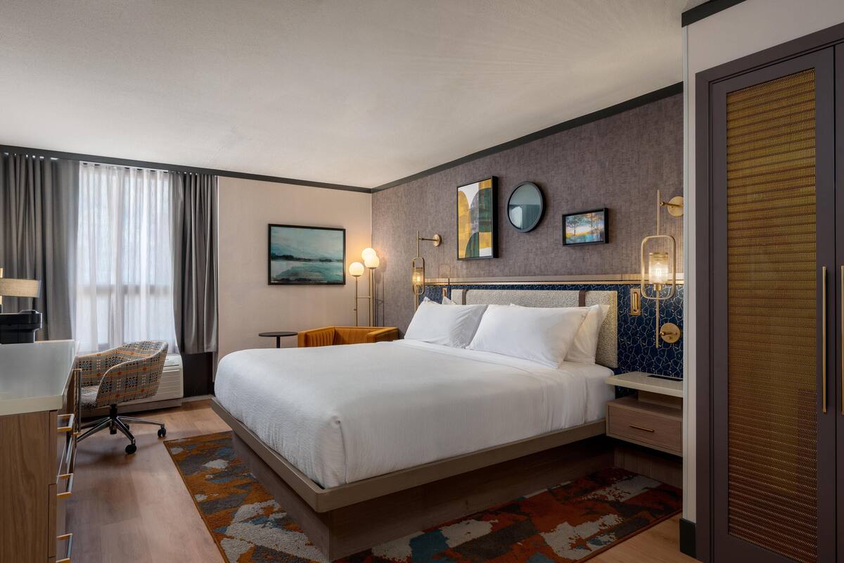 Ein Hotelzimmer mit einem großen Bett, einem Schreibtisch mit Stuhl, einem kleinen Tisch und einem dekorativen Teppich.