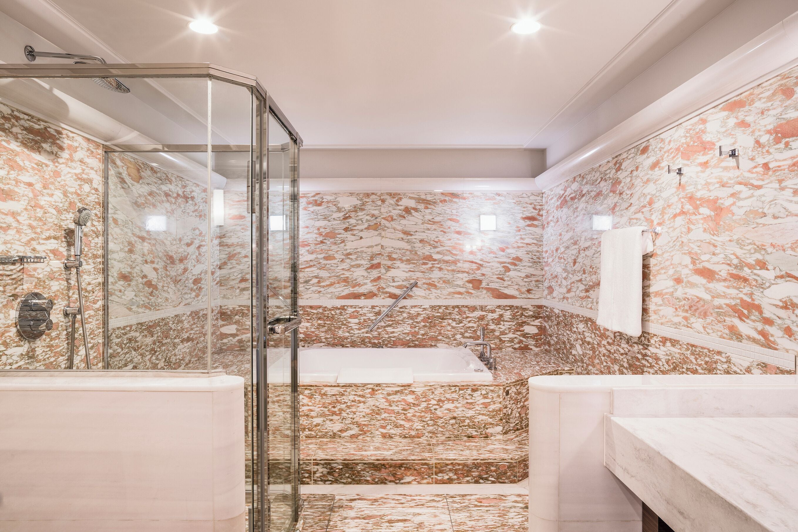 A bathroom with a glass-enclosed shower, a bathtub, and a marble-tiled wall.
