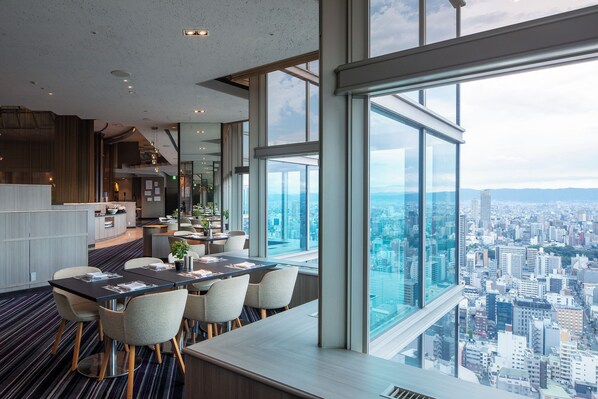 A modern hotel room with a panoramic city view, a dining area with a long table, and a kitchen area. - Swissotel Nankai Osaka (Osaka)