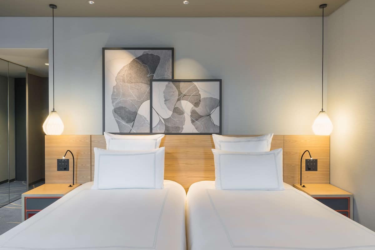 A modern hotel room with two beds, wooden headboard, bedside lamps, and abstract wall art.