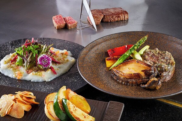 A dining table with two plates of food, one with a steak and vegetables and another with a fish dish and salad. - Swissotel Nankai Osaka (Osaka)