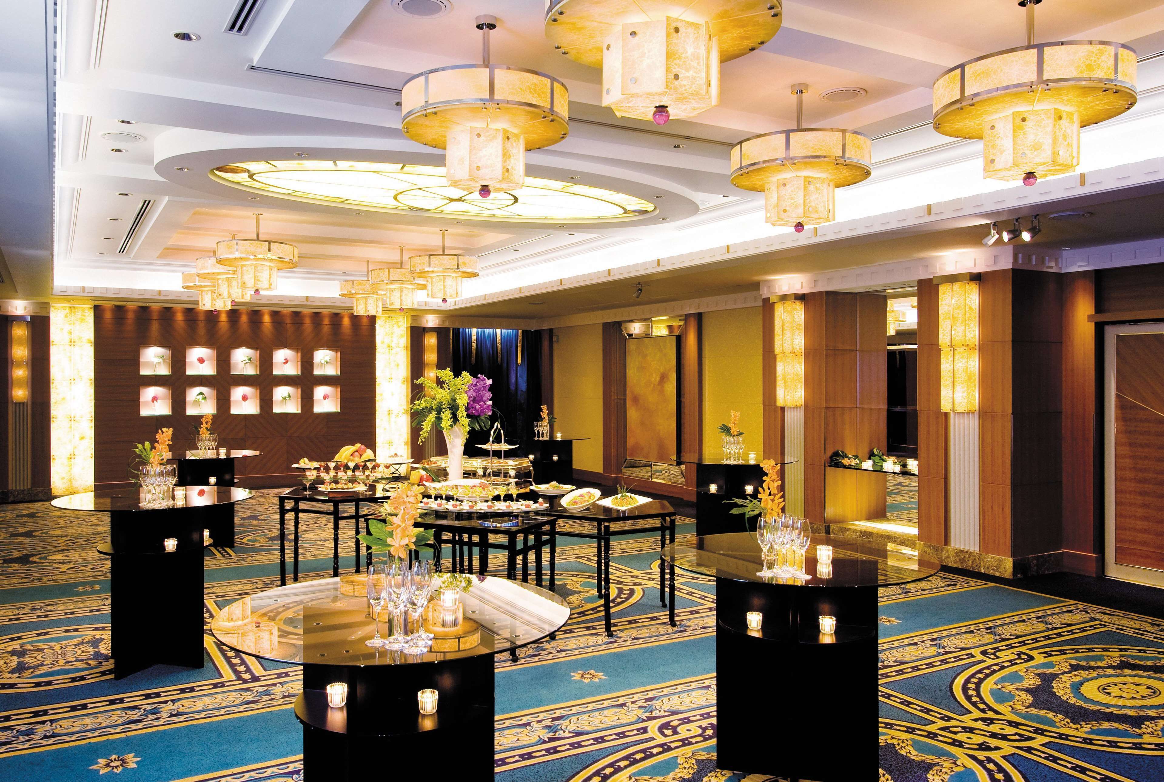 A spacious banquet hall with multiple round tables, elegant chandeliers, and a patterned carpet.