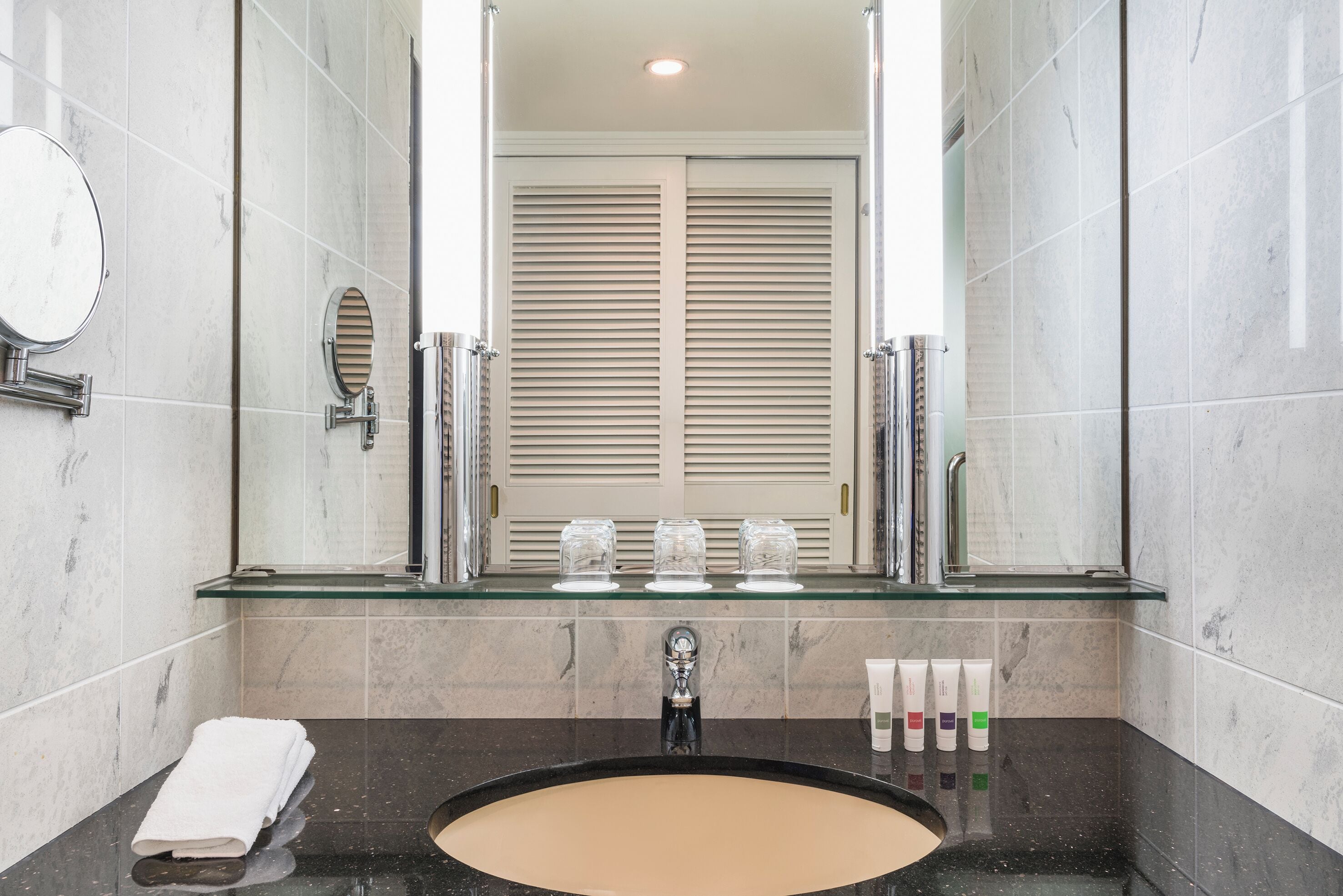 A bathroom with a glass shelf, a sink, a mirror, and a towel.