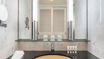 A bathroom with a glass shelf, a sink, a mirror, and a towel.