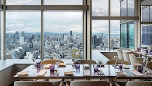 A dining area with tables set for two, large windows offering a cityscape view. - Swissotel Nankai Osaka (Osaka)