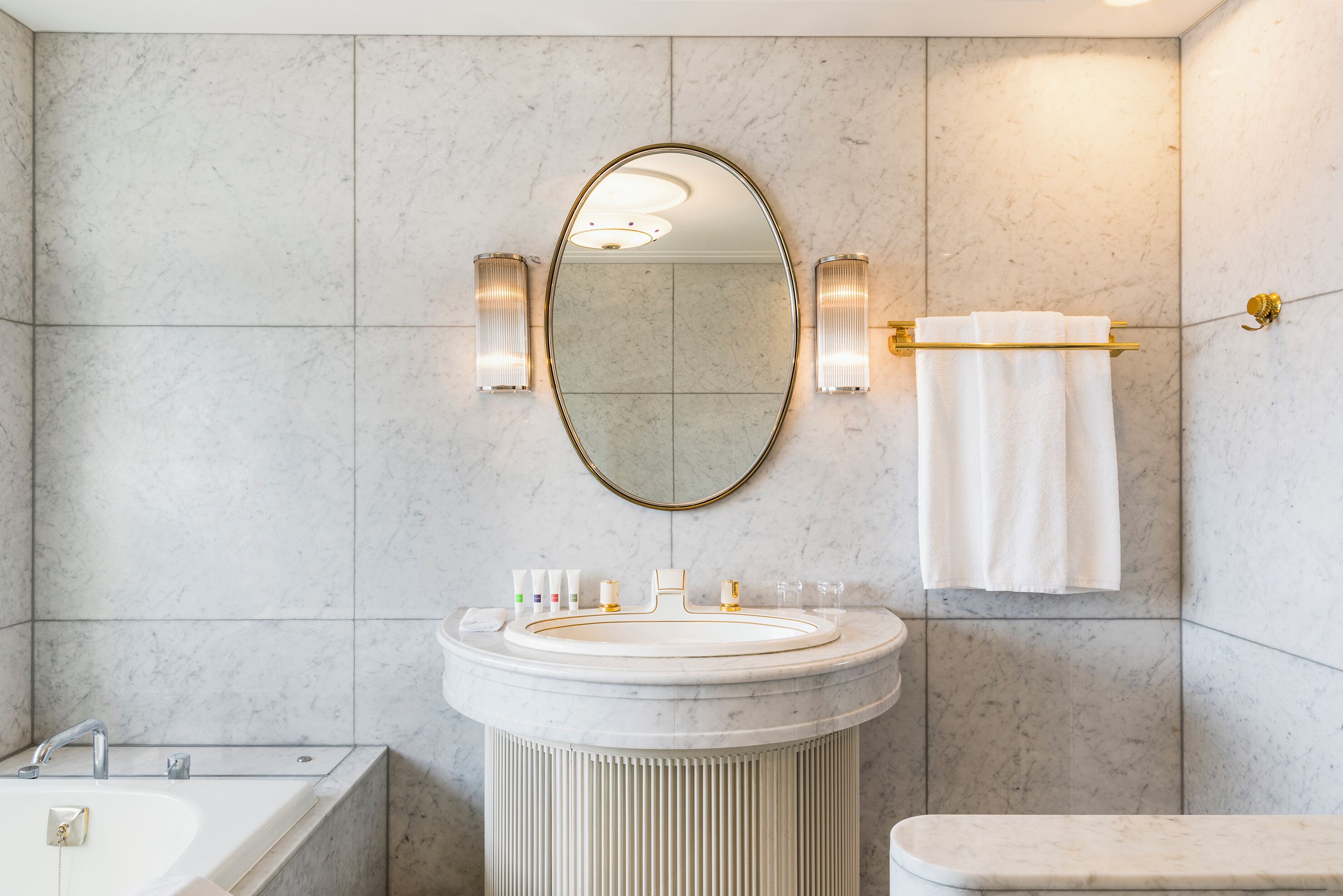 A bathroom with a round sink, a large mirror, two wall sconces, and a towel rack.