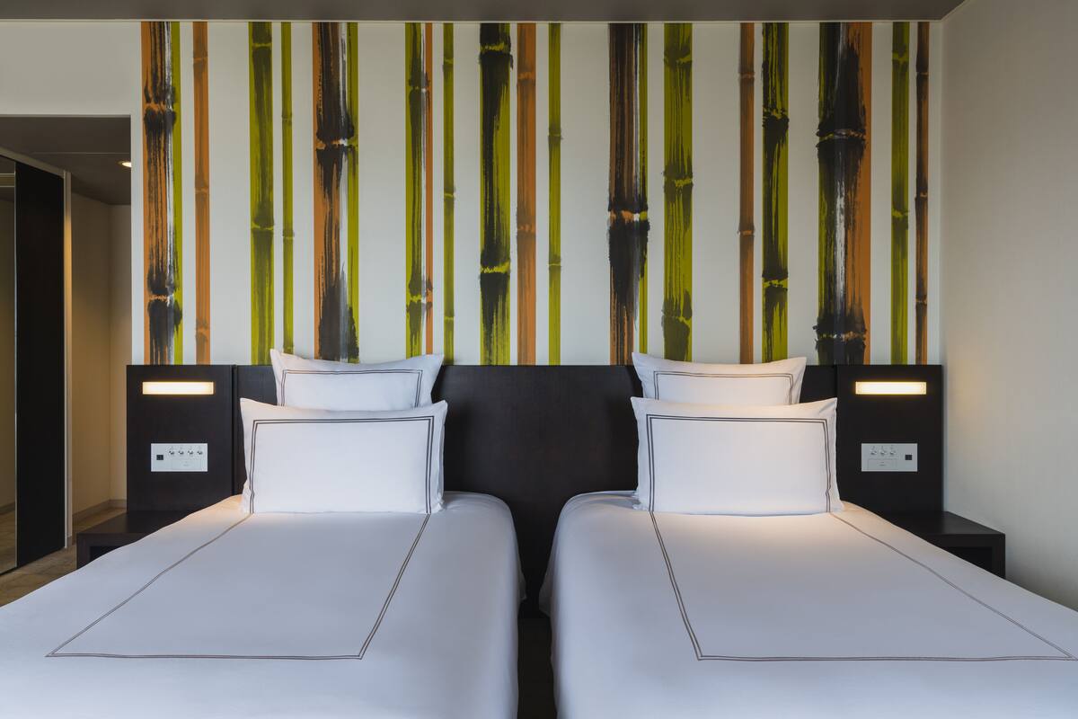 A hotel room with two beds, a wall with vertical stripes, and bedside lamps.