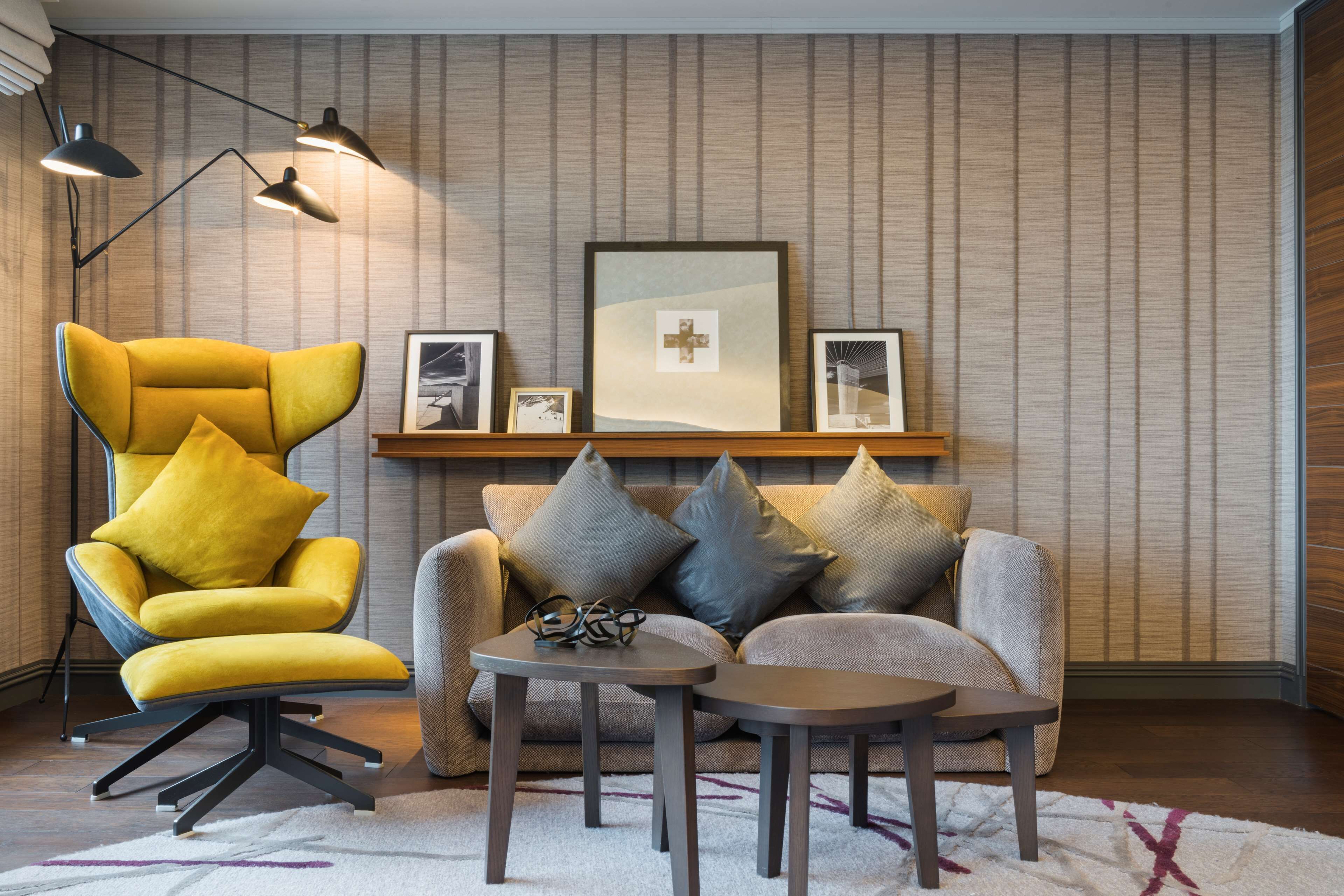 A modern living room with a yellow armchair, a grey sofa, and a small coffee table. There are framed pictures on the wall and a floor lamp.