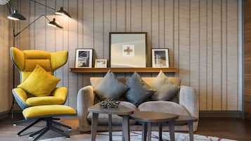 A modern living room with a yellow armchair, a grey sofa, and a small coffee table. There are framed pictures on the wall and a floor lamp.
