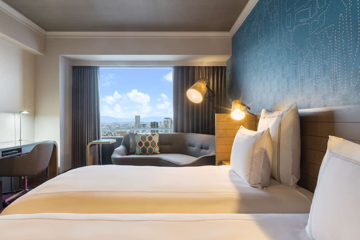A hotel room with a large bed, a desk, a chair, and a view of the city.