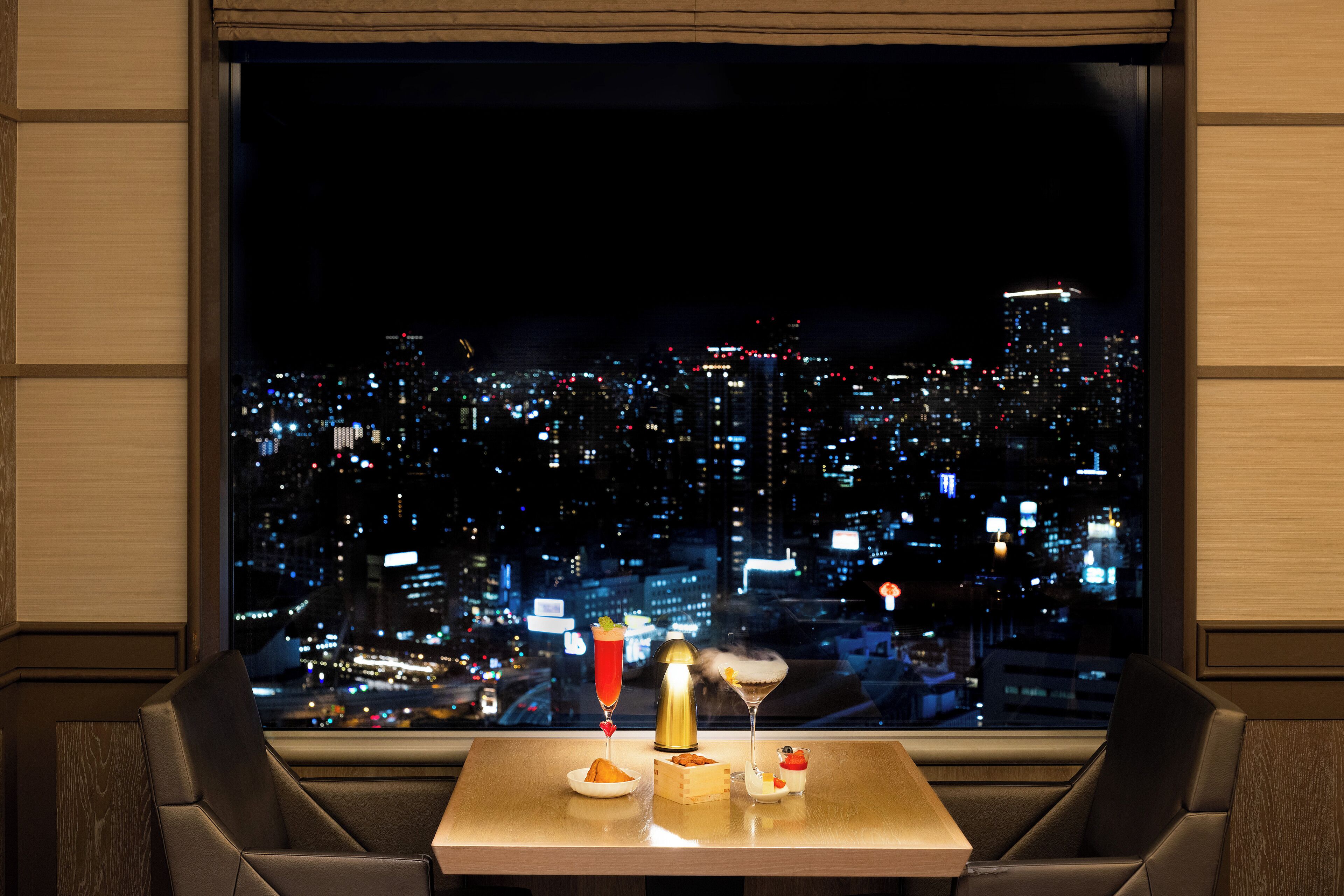A table with a cityscape view, a cocktail, and a dessert.