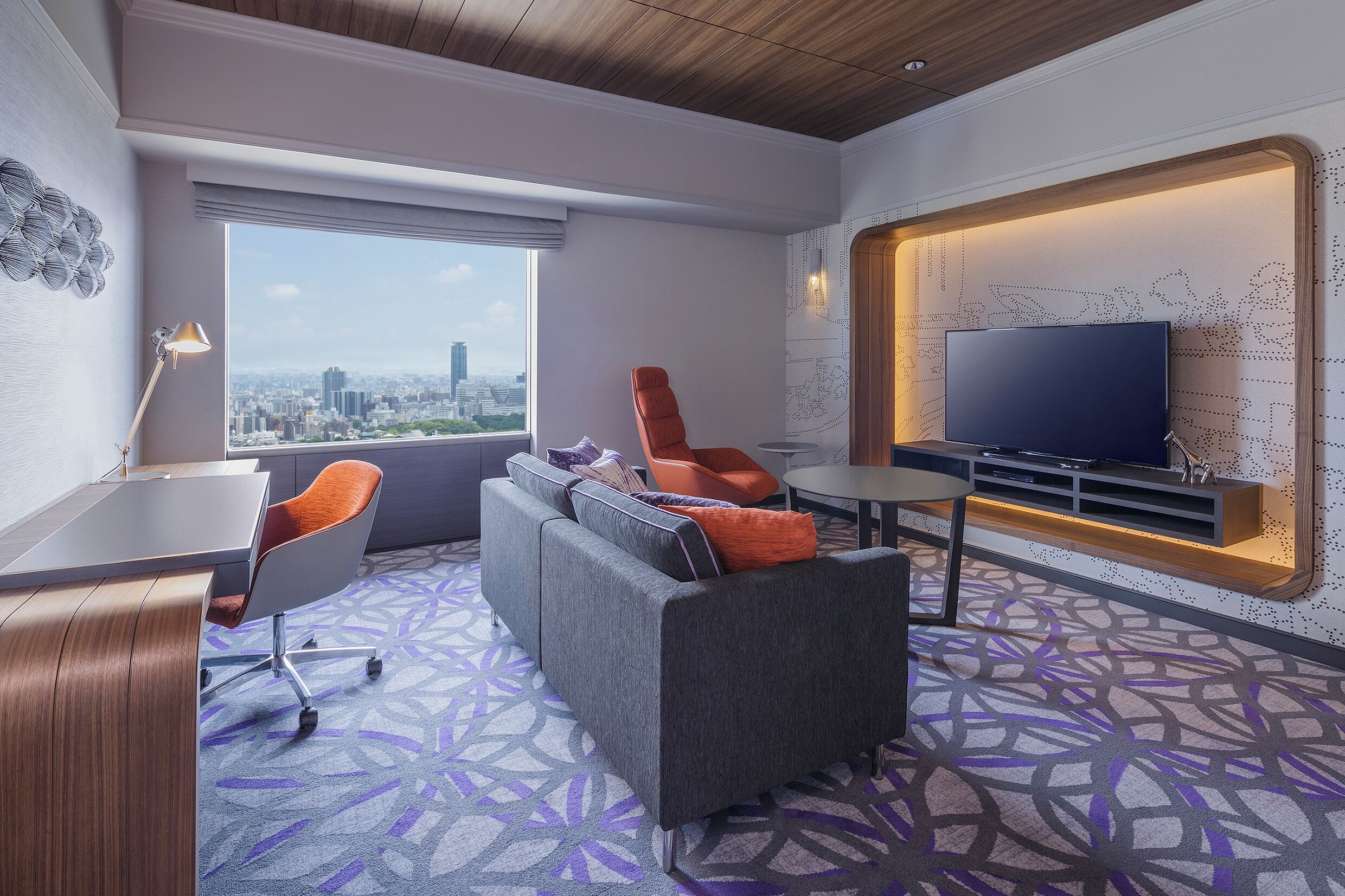 A hotel room with a sofa, a desk, a TV, and a city view.