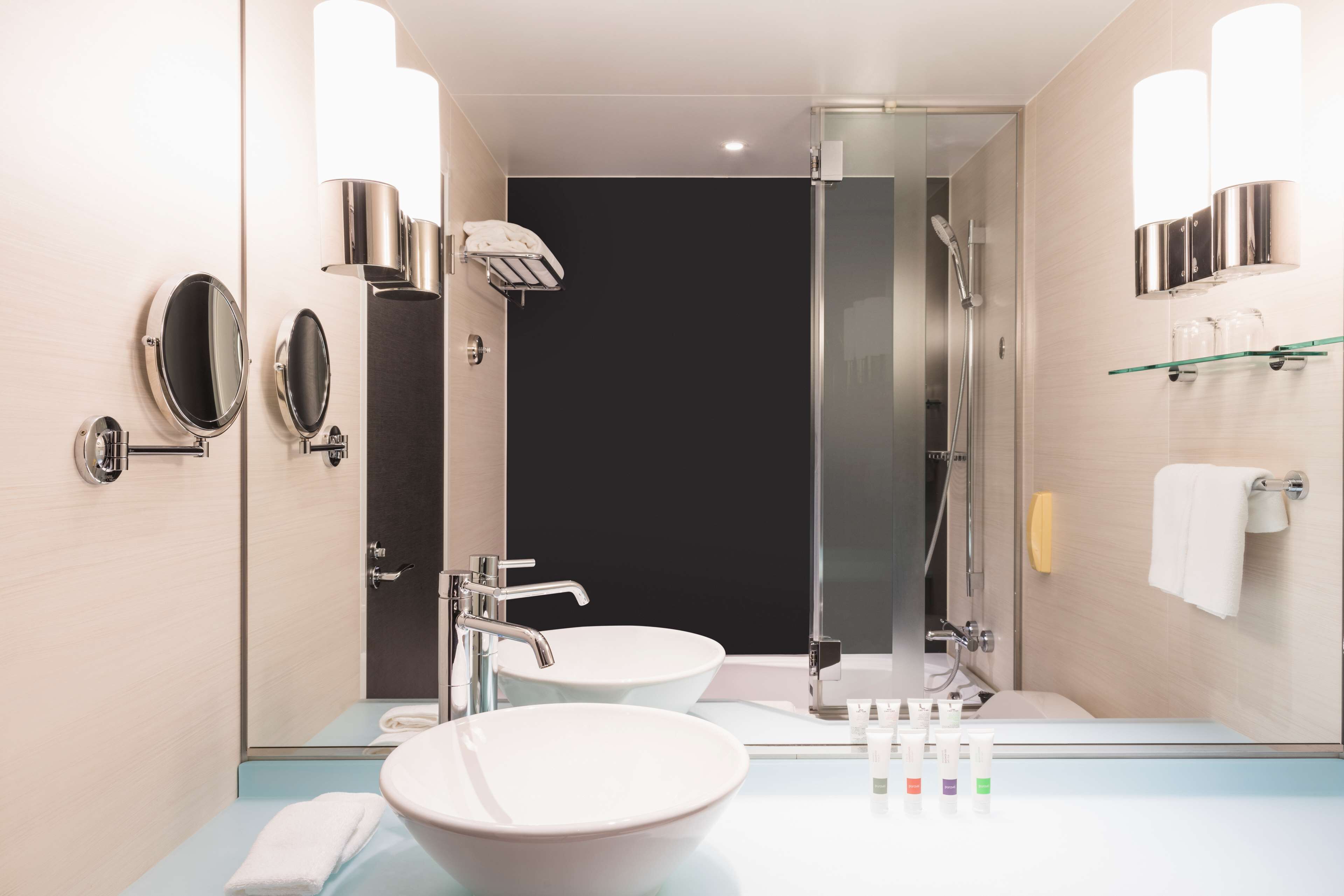 A modern bathroom with two sinks, a glass shower enclosure, and a large mirror.