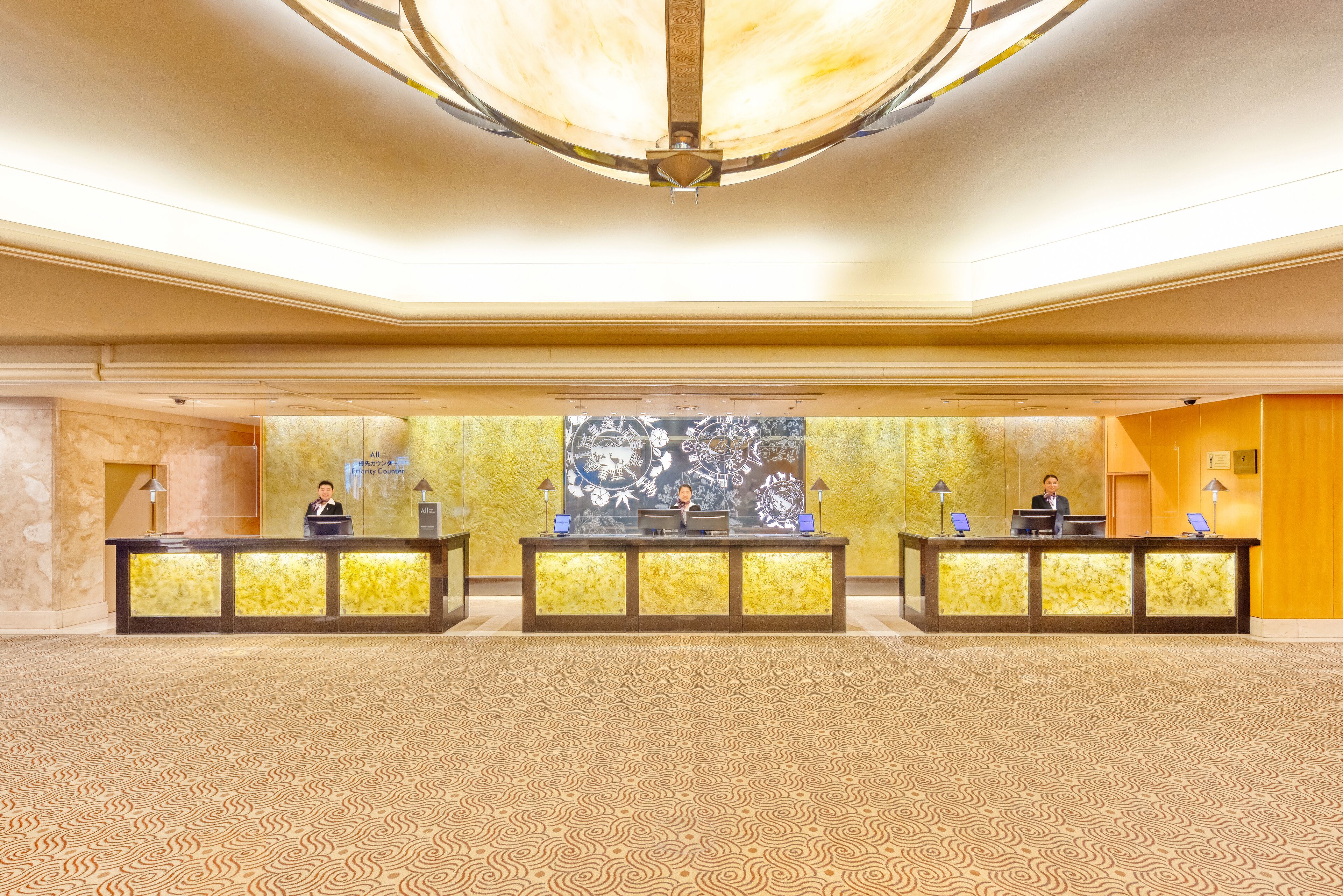 A spacious lobby with a patterned carpet, three reception desks, and a large abstract wall mural.