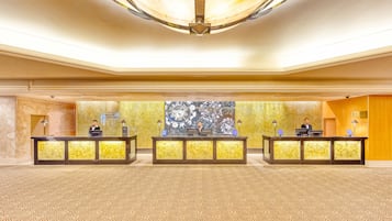 A spacious lobby with a patterned carpet, three reception desks, and a large abstract wall mural.