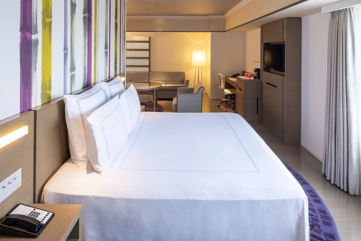 A hotel room with a large bed, a desk, a chair, a TV, and a bathroom.