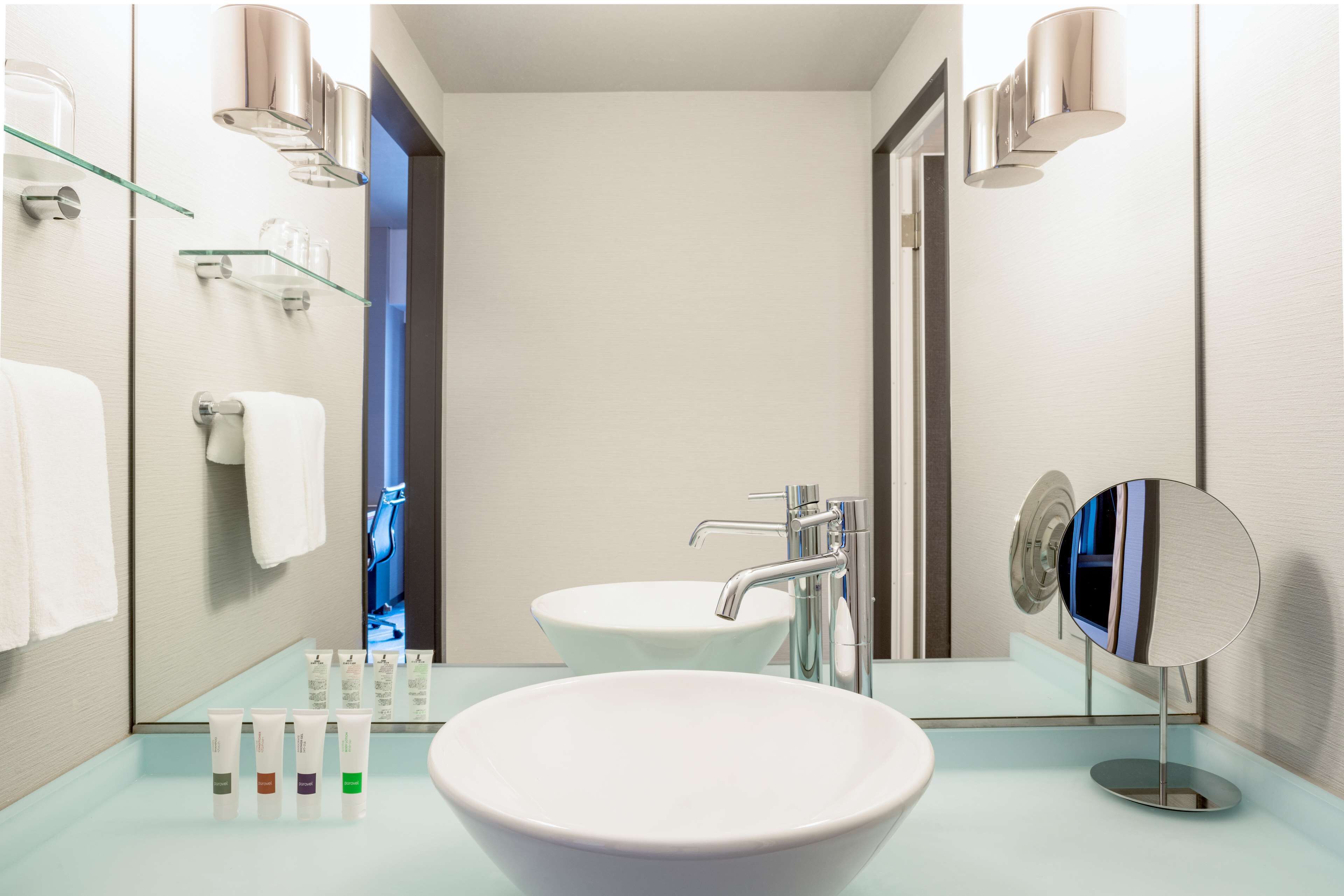 A modern bathroom with a large white sink, a mirror, and a glass shelf with toiletries.