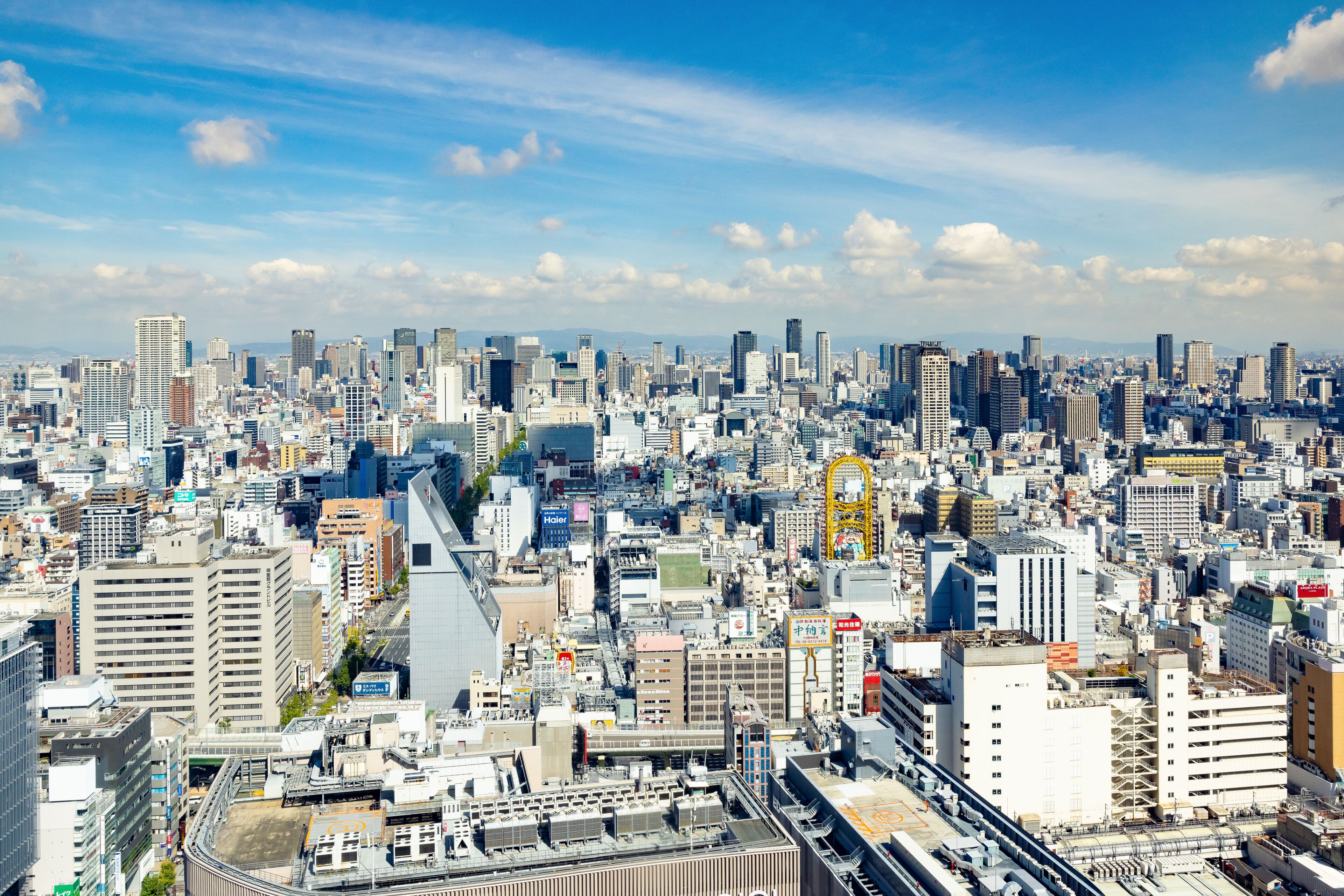 A dense urban cityscape with numerous high-rise buildings, a prominent yellow structure, and a complex network of roads and railways.