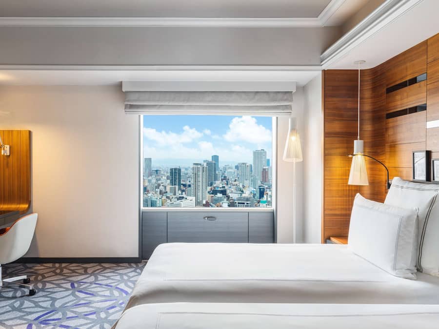 A hotel room with a city view, a bed, a desk, and a chair.