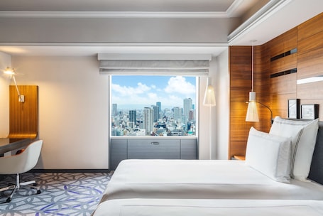 A hotel room with a city view, a bed, a desk, and a chair.