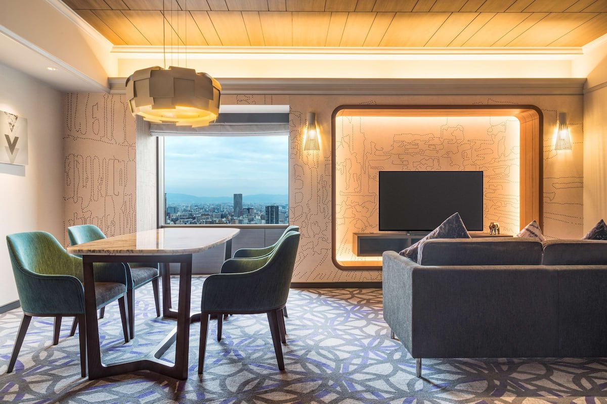 A modern hotel room with a dining area, a sofa, and a TV.