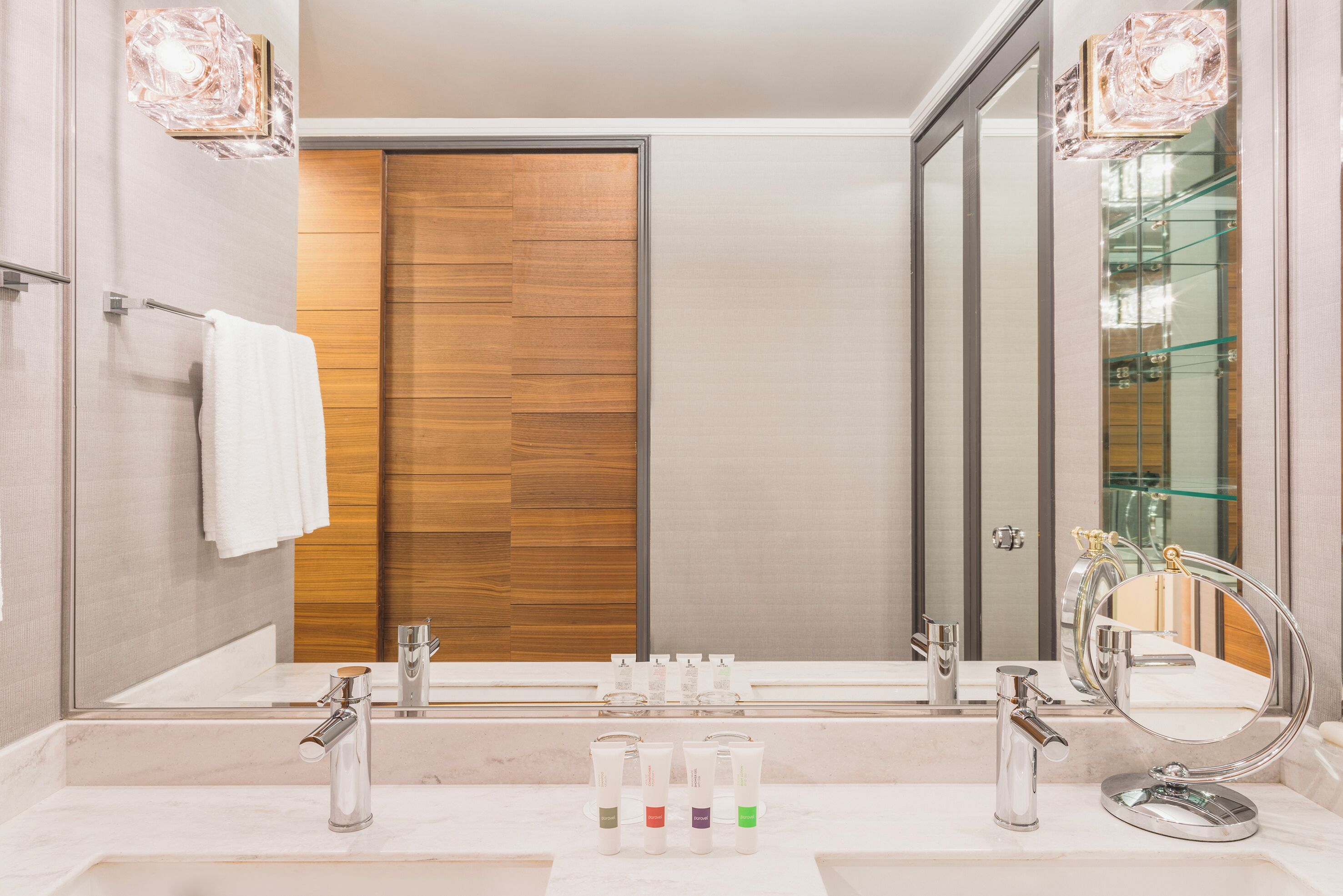 A modern bathroom with a large mirror, two sinks, and a wooden door.