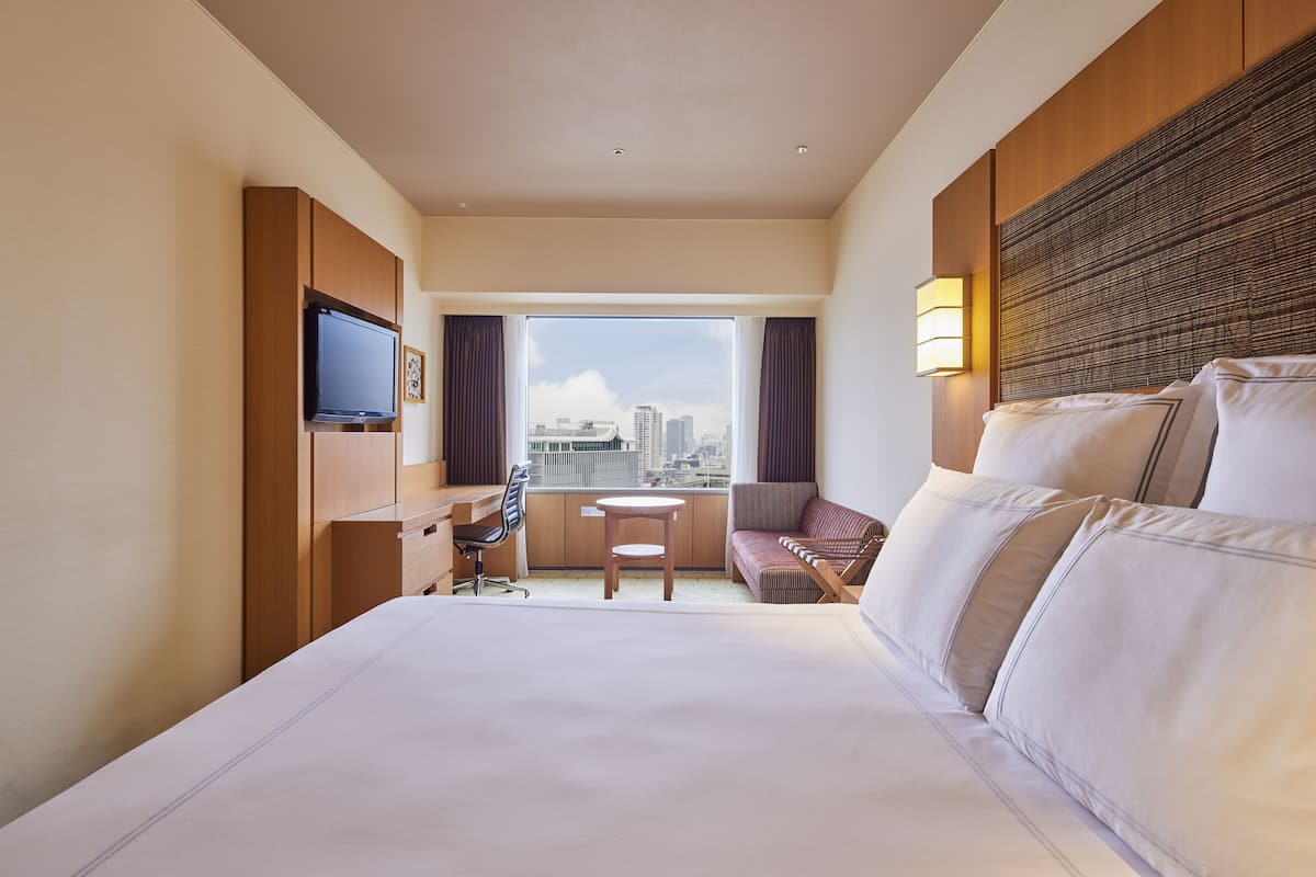 A hotel room with a large bed, a desk, a chair, a small table, and a TV.