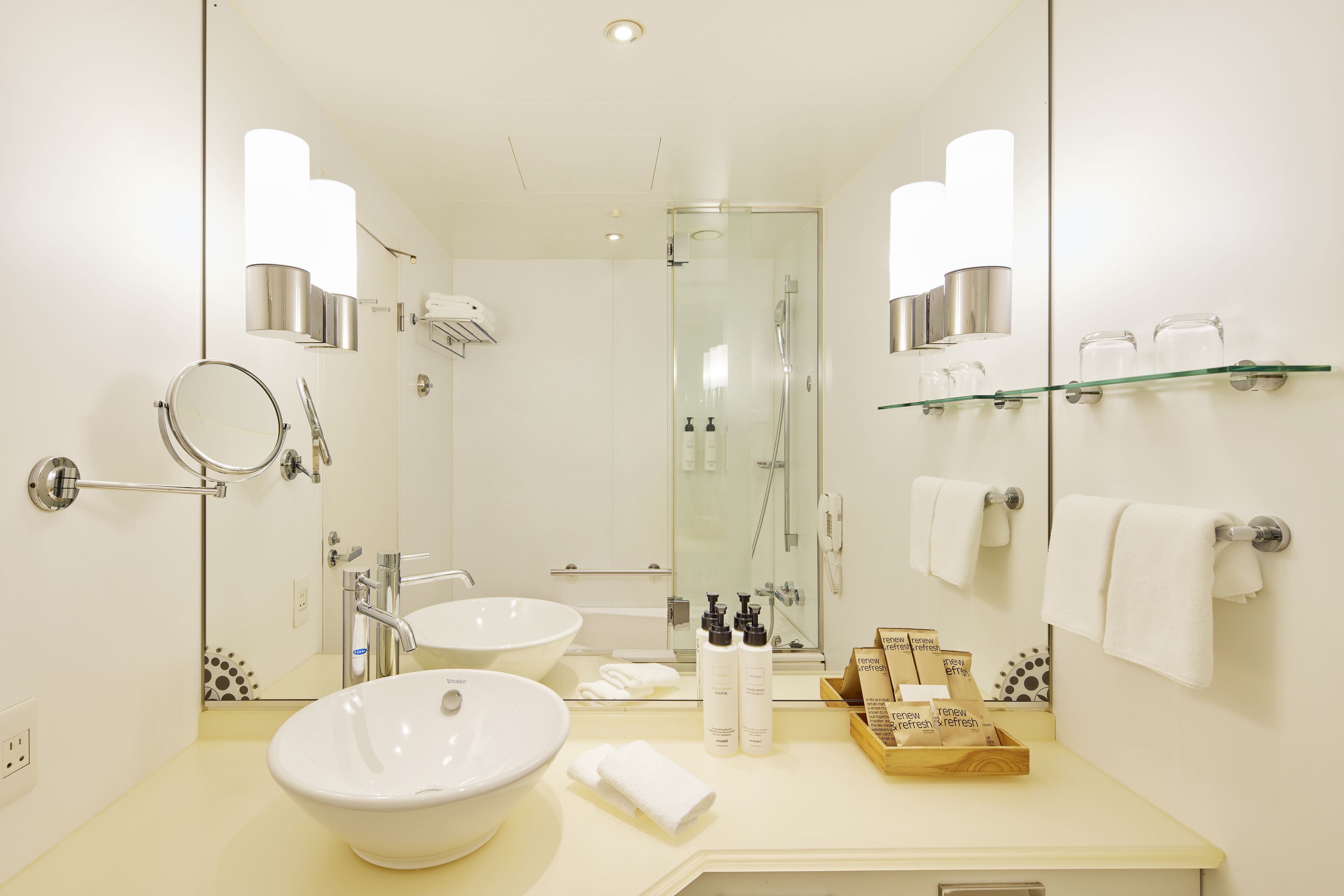 A modern bathroom with a large sink, a glass shower enclosure, and a mirror reflecting the room.