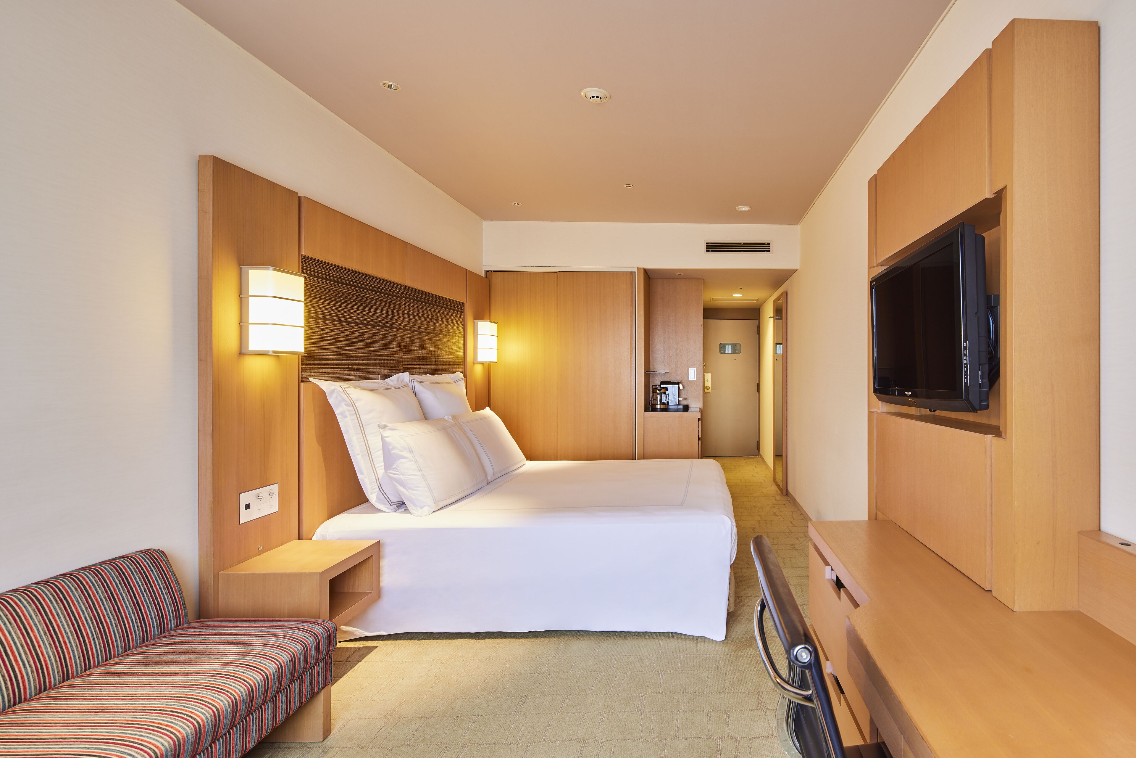Habitación de hotel con cama, mesita de noche, lámpara, televisor y sofá.