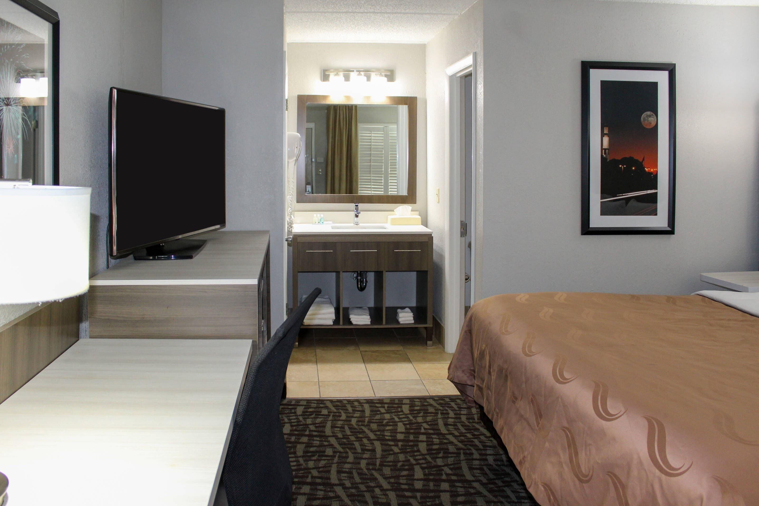 A hotel room with a bed, a TV, a bathroom with a sink and mirror, and a framed picture on the wall.