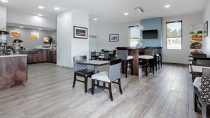 A modern restaurant with a wooden floor, dining area with tables and chairs, kitchen area with appliances, and a TV on the wall.
