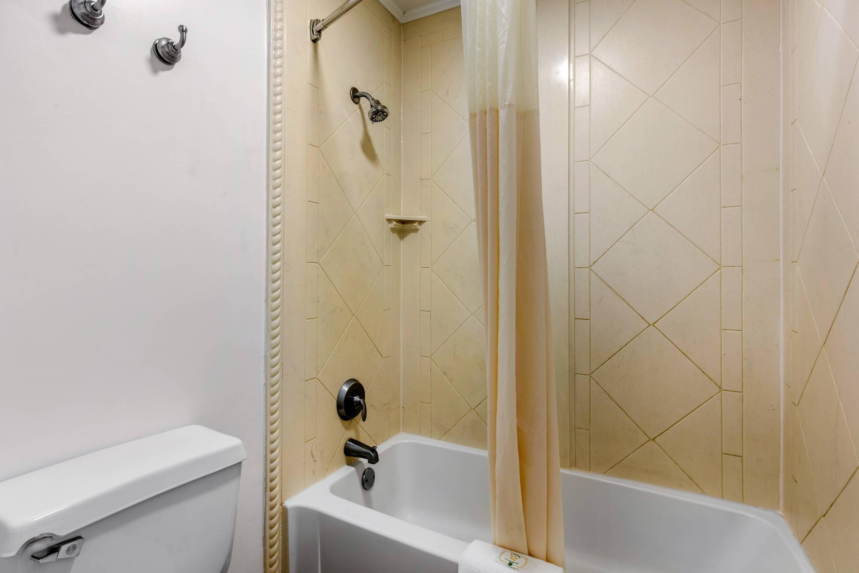 A bathroom with a white bathtub, a showerhead, and a toilet.