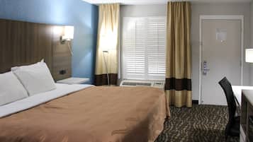 Une chambre d’hôtel avec un grand lit, un bureau, une chaise, une fenêtre avec des rideaux et une lampe fixée au mur.