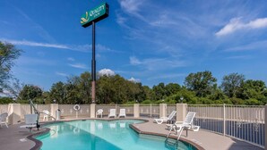 A swimming pool with lounge chairs and a sign for Quality Inn.