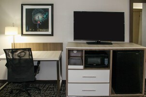 Una habitación de hotel con escritorio, silla, televisor, microondas y refrigerador.
