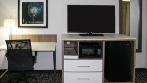 A hotel room with a desk, a television, a microwave, and a refrigerator.