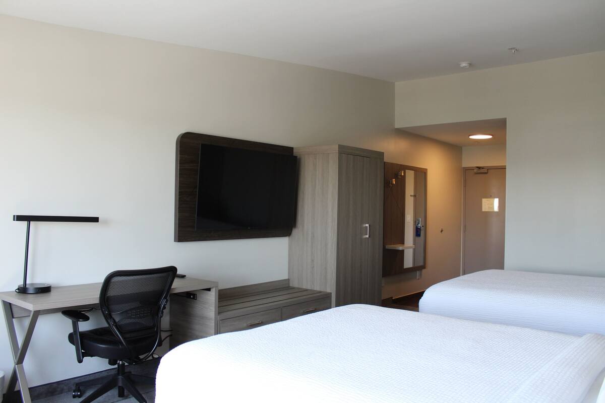 Een hotelkamer met een bureau, stoel, televisie en twee bedden.