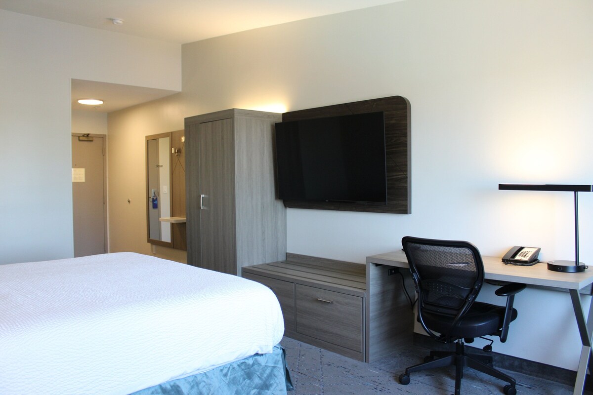 Une chambre d’hôtel comprenant un lit, un bureau avec une chaise, un téléviseur à écran plat et une lampe de bureau.