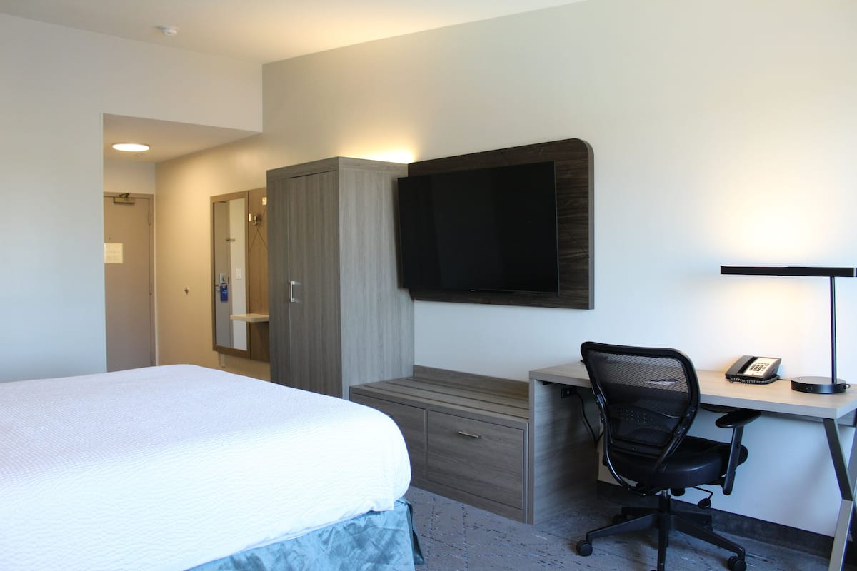 Une chambre d’hôtel comprenant un lit, un bureau avec une chaise, un téléviseur à écran plat et une lampe de bureau.