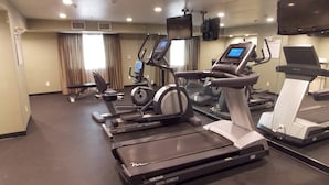 Une salle de sport d’hôtel équipée de tapis de course, de vélos elliptiques et d’un vélo d’appartement.