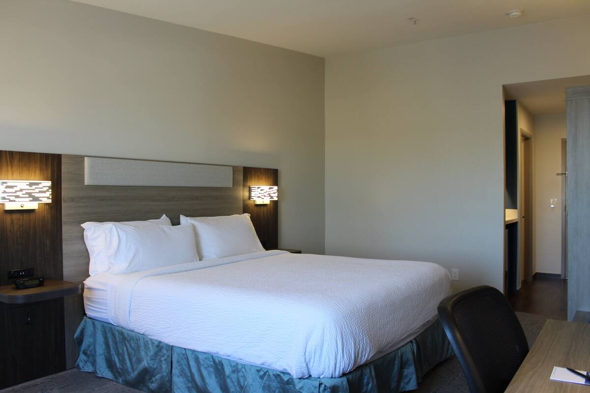 Ein Hotelzimmer mit einem großen Bett, einem Holz-Kopfteil, Nachttischlampen und einem Schreibtisch mit Stuhl.