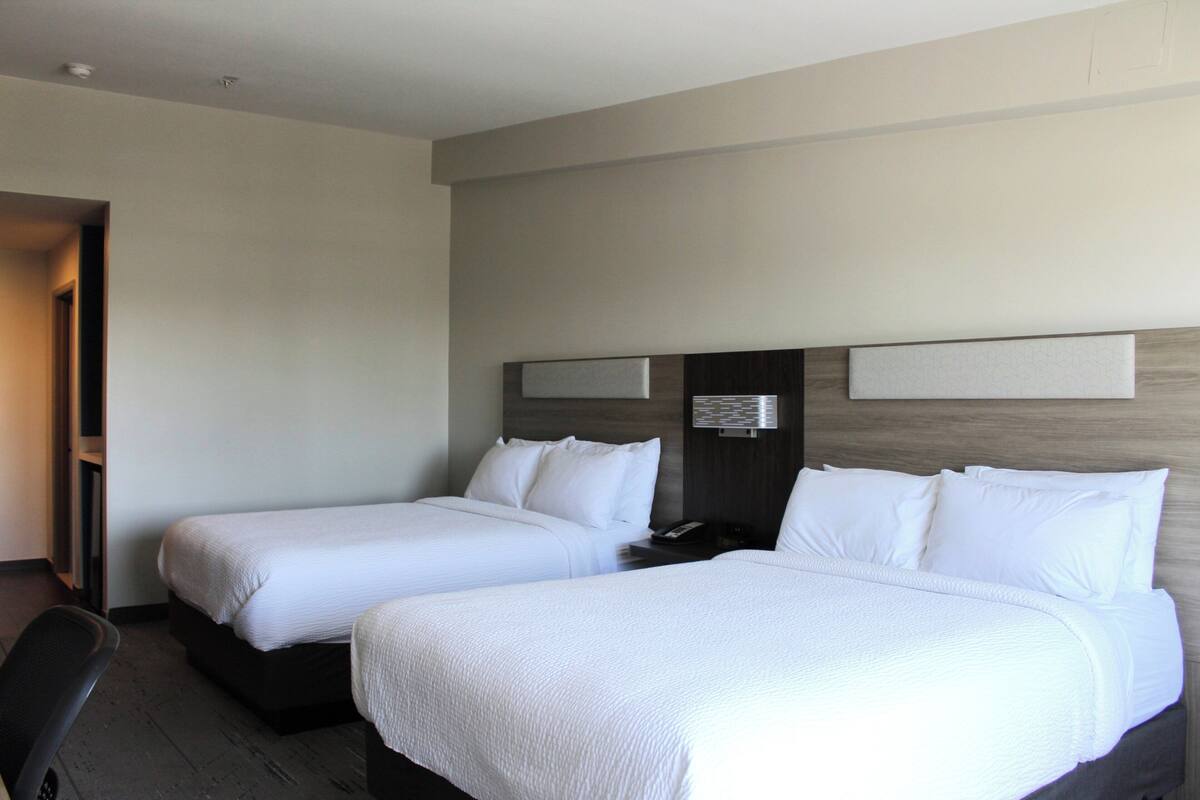 A hotel room with two single beds, a desk, and a chair.