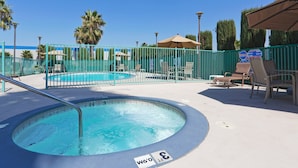 Un espace piscine comprenant un jacuzzi, des chaises longues et une piscine entourée d’une clôture.