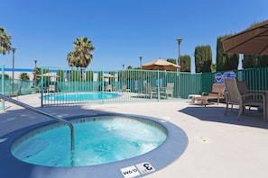 Un espace piscine comprenant un jacuzzi, des chaises longues et une piscine entourée d’une clôture.