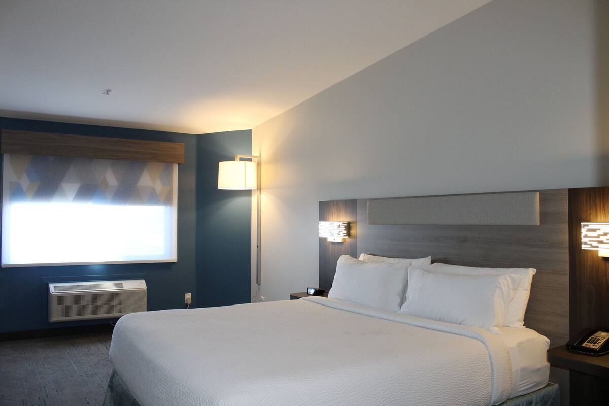 Een hotelkamer met een groot bed, nachtlampjes, een nachtkastje en een raam met jaloezieën.