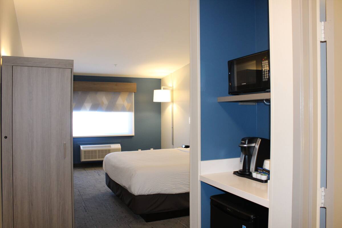 Een hotelkamer met een bed, een magnetron, een koffiezetapparaat en een kledingkast.