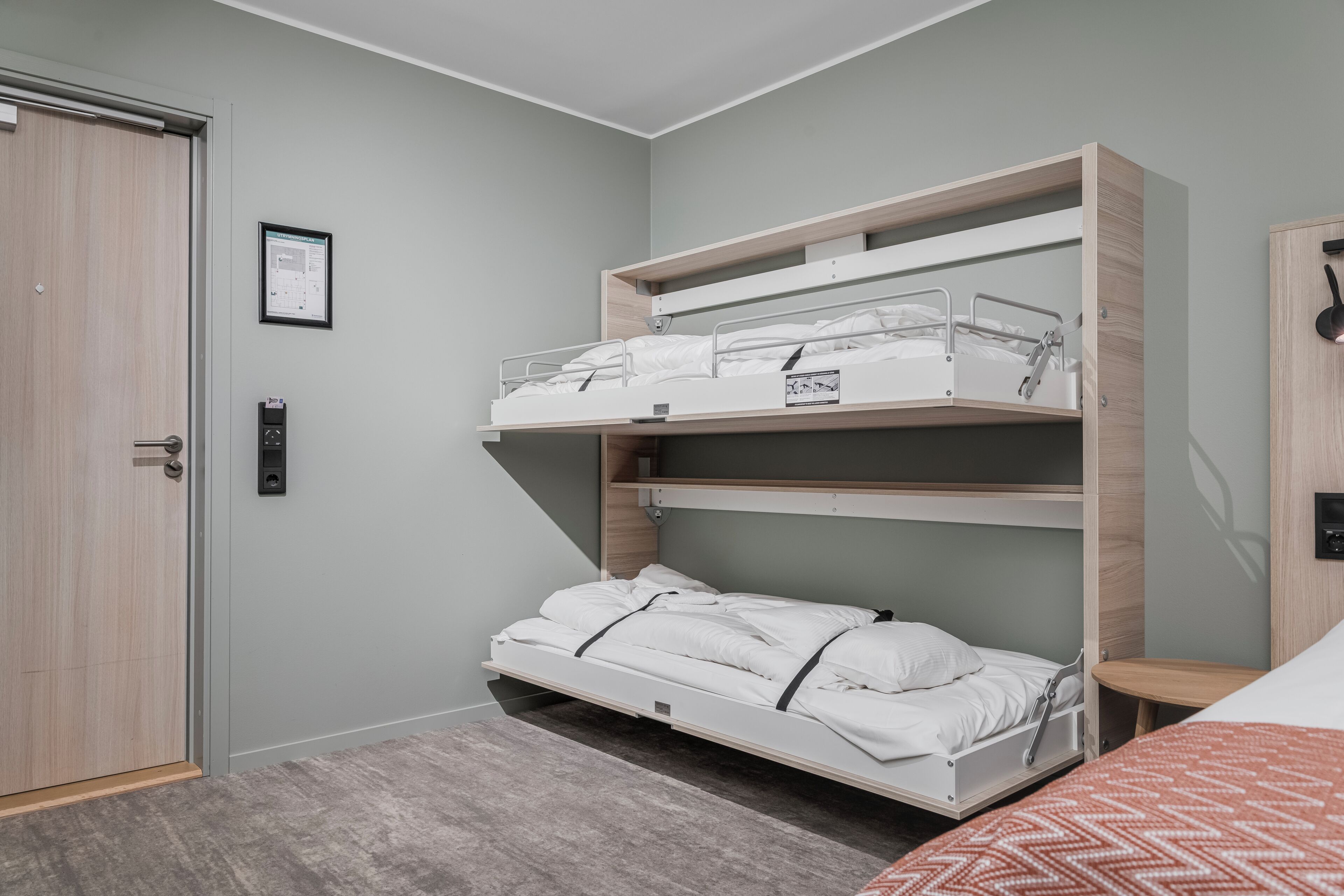 Een kamer met een stapelbed, een deur, een kleine tafel en een wandlamp.